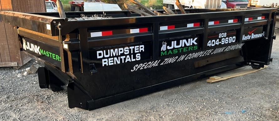 Large black dumpster with "junk masters" branding and contact information, specializing in dumpster rentals, placed on a construction site.