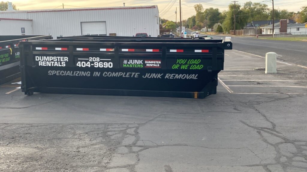 A dumpster labeled with "dumpster rentals" and contact information placed on an asphalt surface.